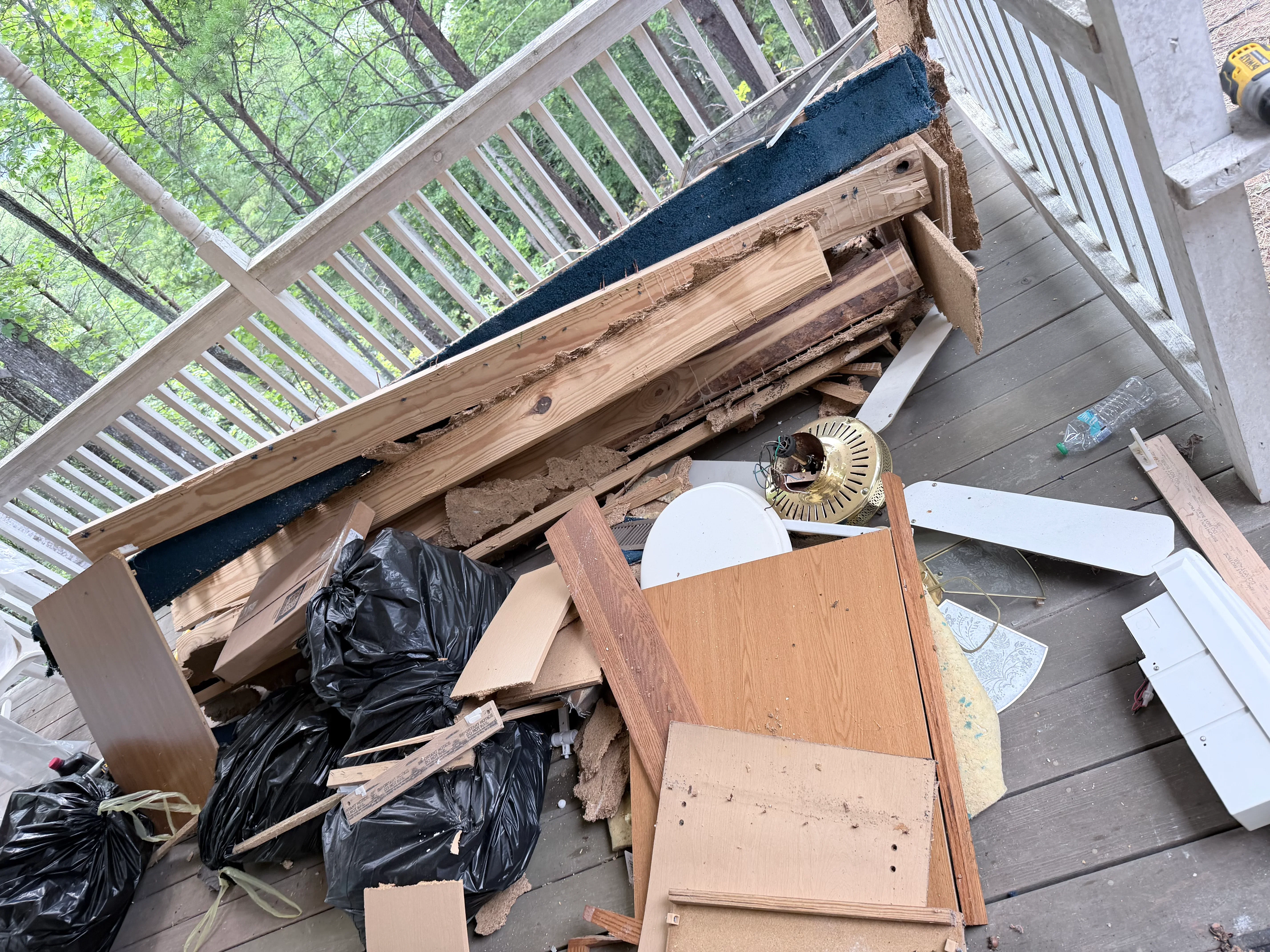 Deck cluttered with junk removal debris including wood, bags, and furniture before cleanup